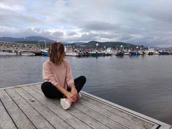 Woman sitting on pier over lake against sky