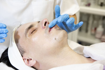 Beautician's hands applying an exfoliating scrub to a middle-aged man's lips