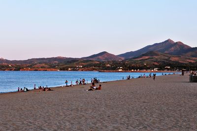 People on beach against clear blue sky