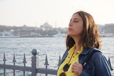 Woman with closed eyes against river in city