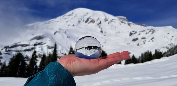 Close-up of woman hand holding snowcapped mountain against sky