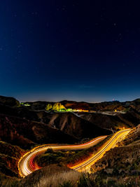 Aerial view of light trails on mountain road against sky at night