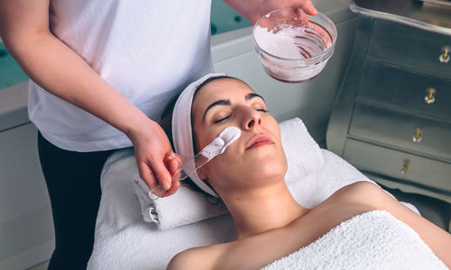 Beautician applying facial pack on customer face at spa