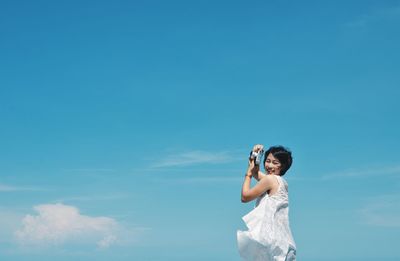 Low angle view of woman photographing against blue sky