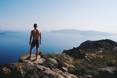 Rear view of shirtless man standing on rock against sea