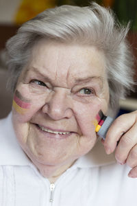 Portrait of confident senior woman painting german national colors on her cheek