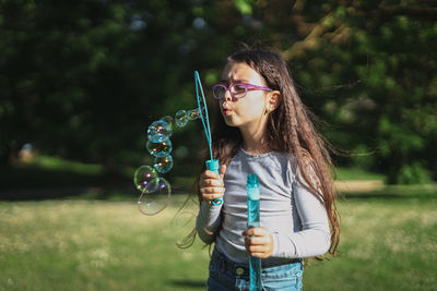 Portrait of a beautiful caucasian girl blows soap bubbles standing in the park