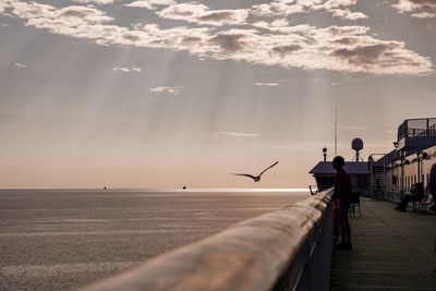 People on pier by sea against sky