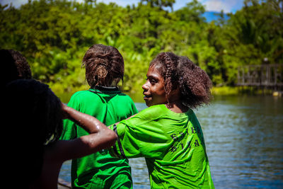 Smiling girl with friends standing by lake in forest