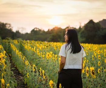 Side view of woman standing on field against sky during sunset