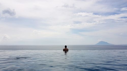 Rear view of man by sea in infinity pool