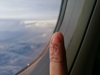 Close-up of hand against sky seen through airplane window