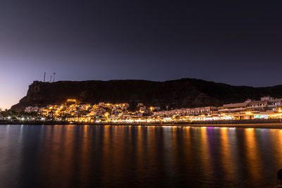 Illuminated city by sea against clear sky at night