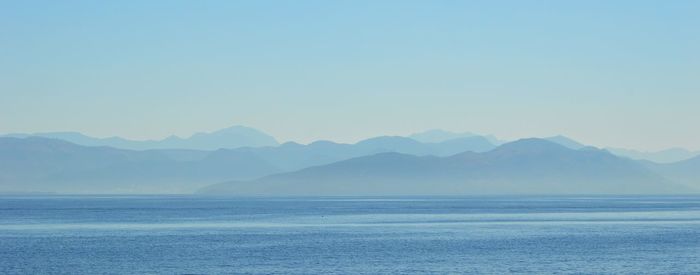 Scenic view of sea and mountains against clear blue sky