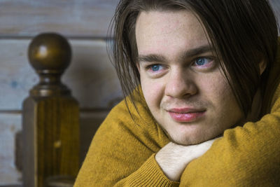 Close-up of smiling young man wearing sweater looking away while leaning on wooden railing at home