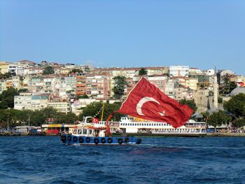 Sailboats in sea by buildings against clear blue sky