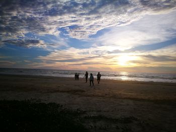 Silhouette people standing on beach against sky during sunset