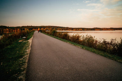 Road by lake against sky during sunset