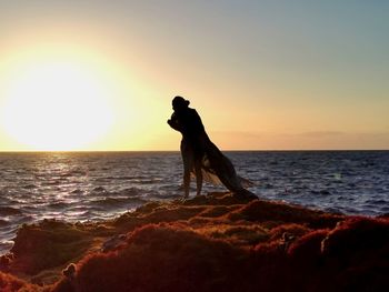 Silhouette man standing on rock at beach against sky during sunset