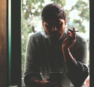 Man using mobile phone against window