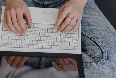 Attractive young woman working from home - female entrepreneur sitting on sofa with laptop computer and checking cell phone from comfort of home