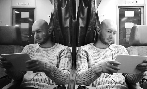 Reflection of man using digital tablet while traveling in train