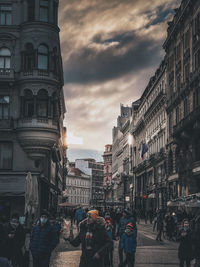 People on street amidst buildings in city against sky