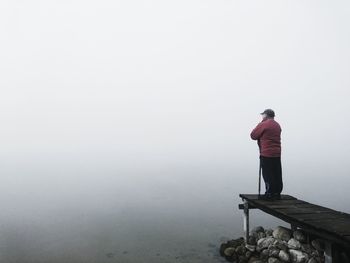 Rear view of man standing by water against sky