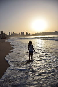 Rear view of woman standing on beach during sunset