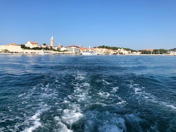 Scenic view of sea by buildings against clear blue sky