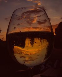 Close-up of beer glass against sunset sky