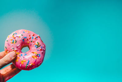 Cropped hand holding donut against blue background