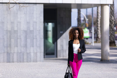 Portrait of fashionable young woman standing against building in city