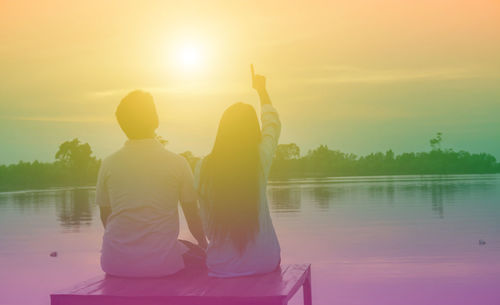 Rear view of people on lake against sky during sunset