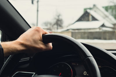 Selective focus man's hand on steering wheel, driving car in winter background. travel background