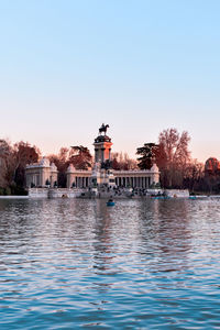 Buildings by river against clear blue sky