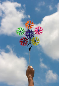 Cropped hand holding colorful pinwheel toy against sky