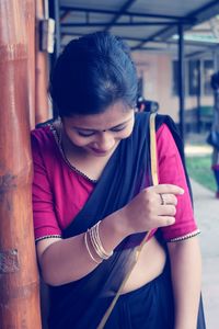 Woman wearing sari while standing by wooden pole