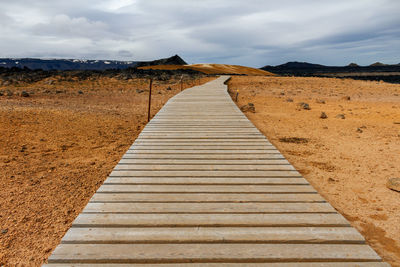 Boardwalk leading towards mountain against sky