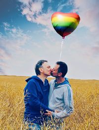 Men and balloons on field against sky