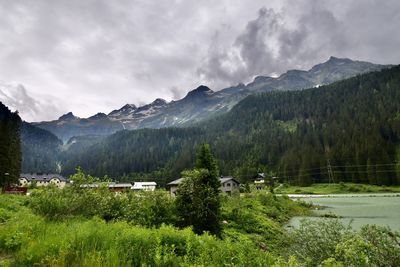 Scenic view of small village and landscape with lake in the mountains against cloudy sky