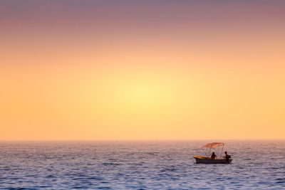 Scenic view of sea and boat with couple against sky during sunset