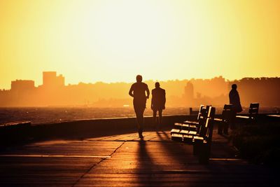 Silhouette people standing on shore against sky during sunset