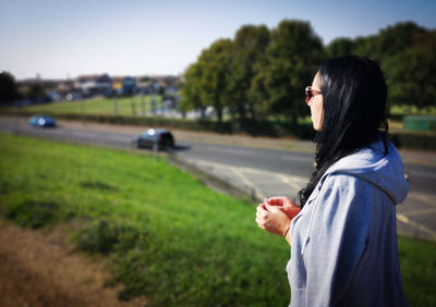 Side view of woman standing against trees in city