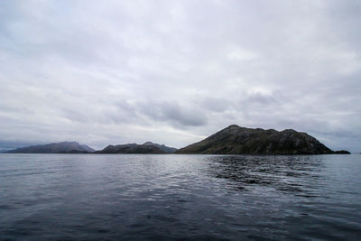 Scenic view of sea by mountain against sky
