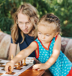 Mother looking at girl playing chess in yard