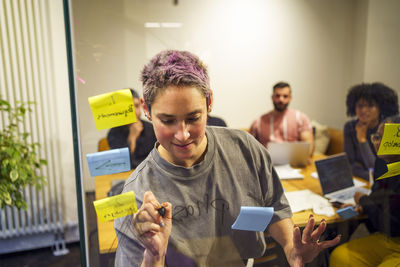Non-binary business professional writing on glass wall in meeting room at tech startup office