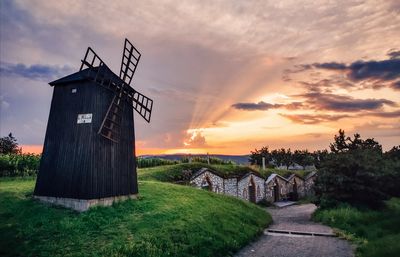 Traditional windmill on field against sky during sunset