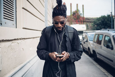 Young man with in-ear headphones using mobile phone on footpath