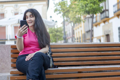 Young lifestyle city people sitting on a street bench using their mobile phone on video call. 